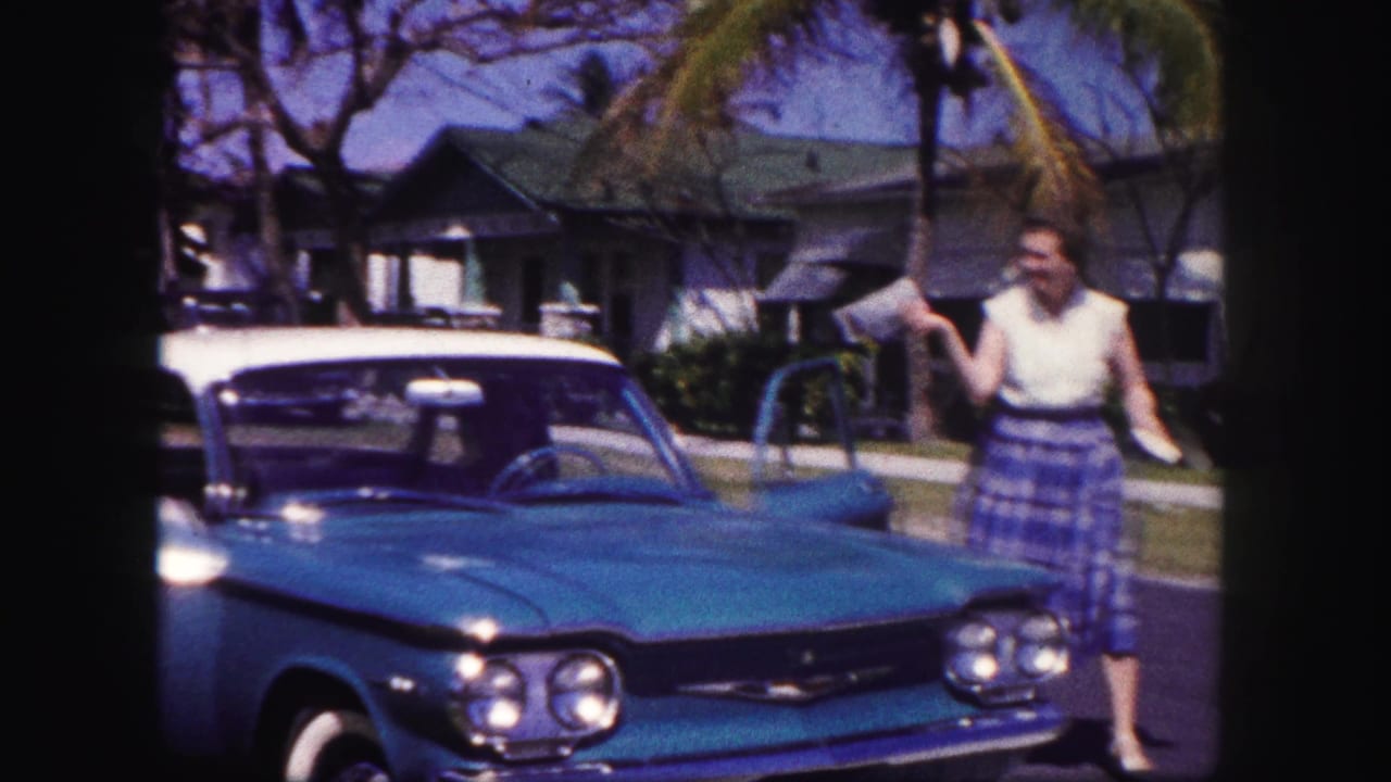 A turquoise-and-white car is parked with doors open as a woman stands nearby in 1960 Tampa home-movie footage.