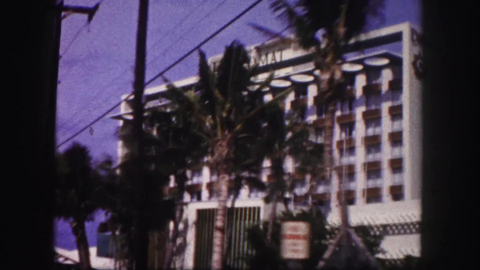 A large Tampa-area building appears beyond palm trees and overhead wires in the final 1960 home-movie frame.