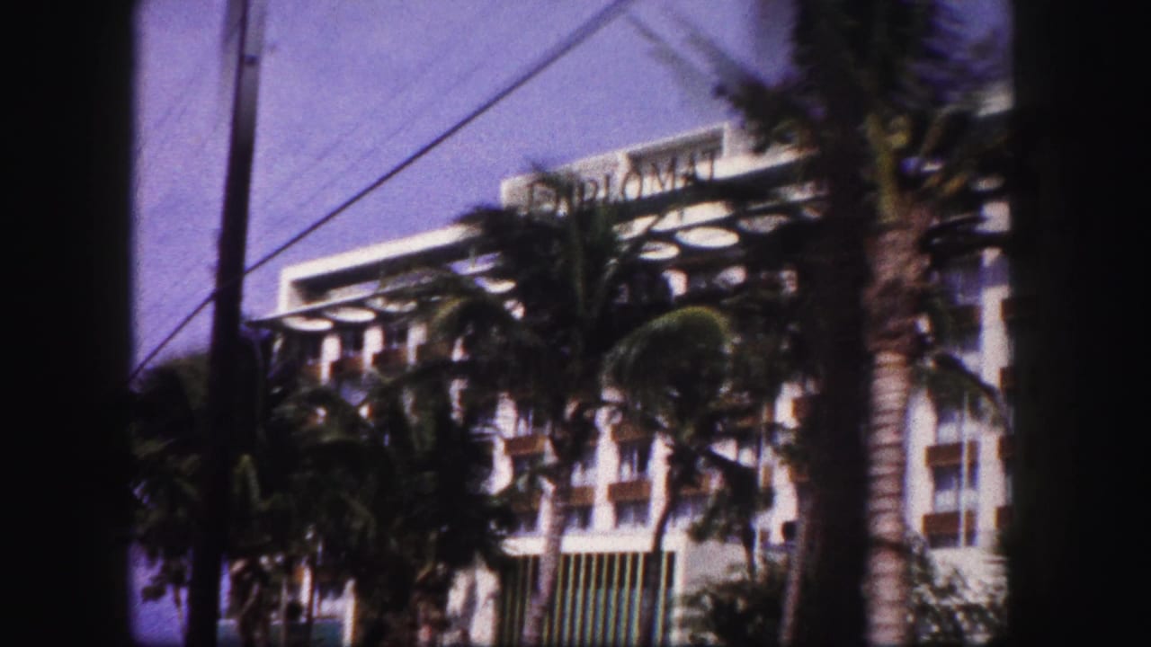 1960 Tampa hotel exterior seen through palms, with balconies, overhead wires, and dark 8mm frame edges.