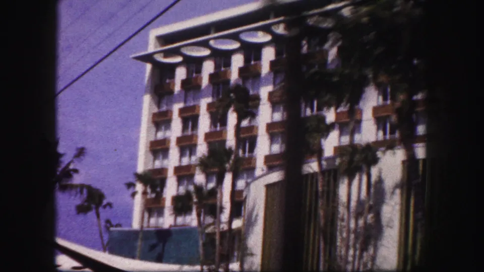1960 Tampa street view of a white hotel with repeating balconies, palms, overhead wire, and a low angular canopy.