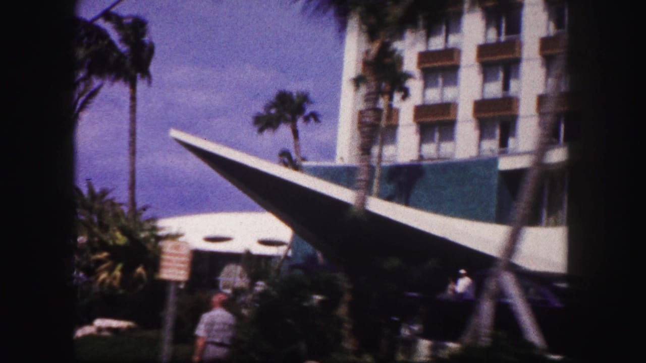 1960 Tampa hotel exterior with a sharp angled canopy, palm trees, multi-story balconies, and distant visitors near the entrance.