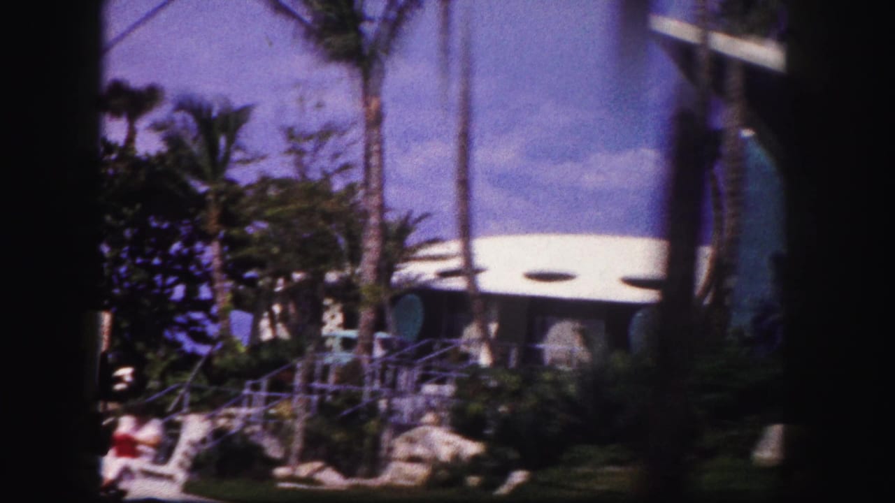 Tampa hotel grounds in 1960 showing a curved white entrance, palms, steps, railings, landscaping, and visitors at a distance.