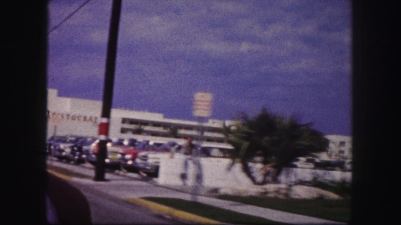 A moving 8mm view in Tampa shows the Aristocrat building, parking lot, palms, street pole, and several cars.