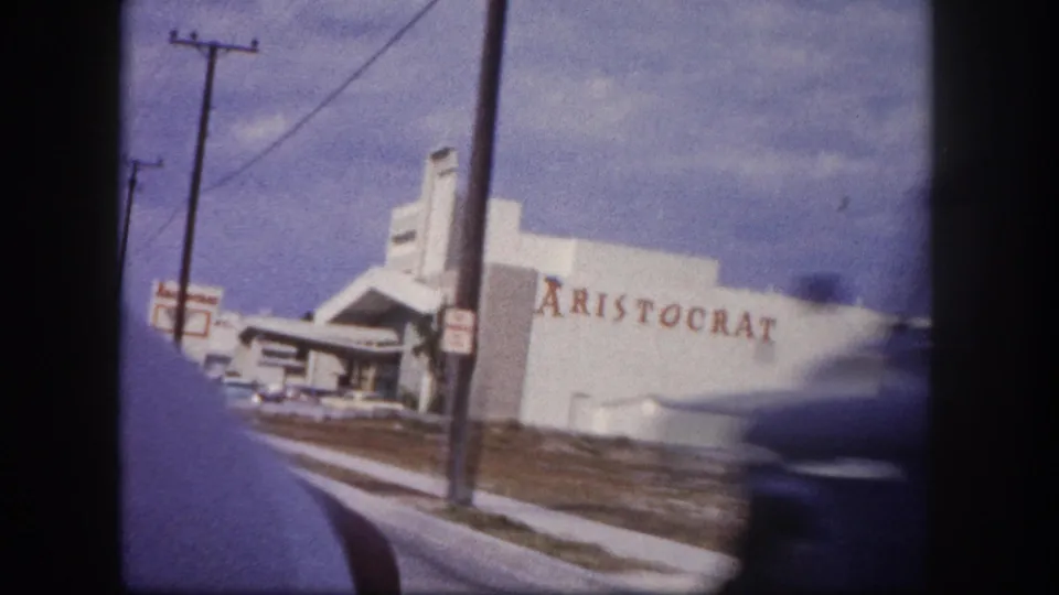 1960 Tampa drive-by frame showing the ARISTOCRAT building closer to camera with motion blur from a passing vehicle.