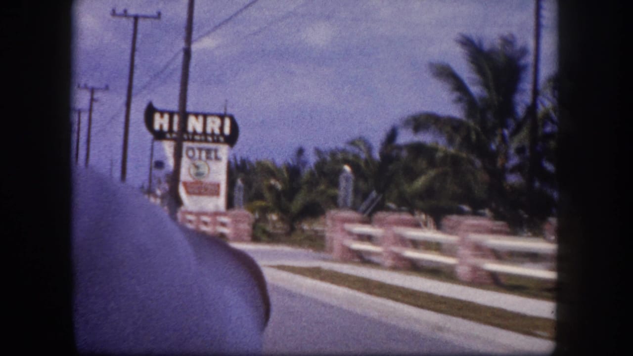 1960 Tampa car-window view approaching the Henri Apartments Motel sign with railings, palms, utility poles, and road edge visible.