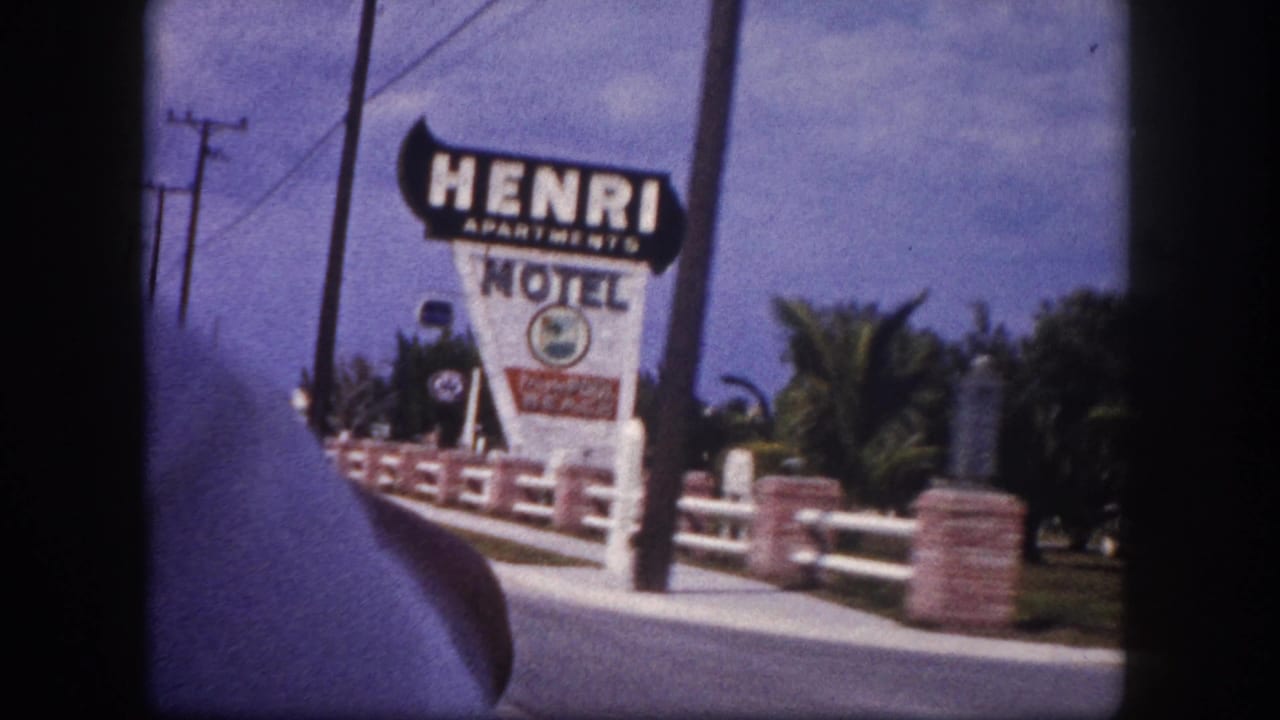 The Henri Apartments Motel sign stands near brick-and-white roadside railings in a 1960 Tampa drive-by view from inside a car.