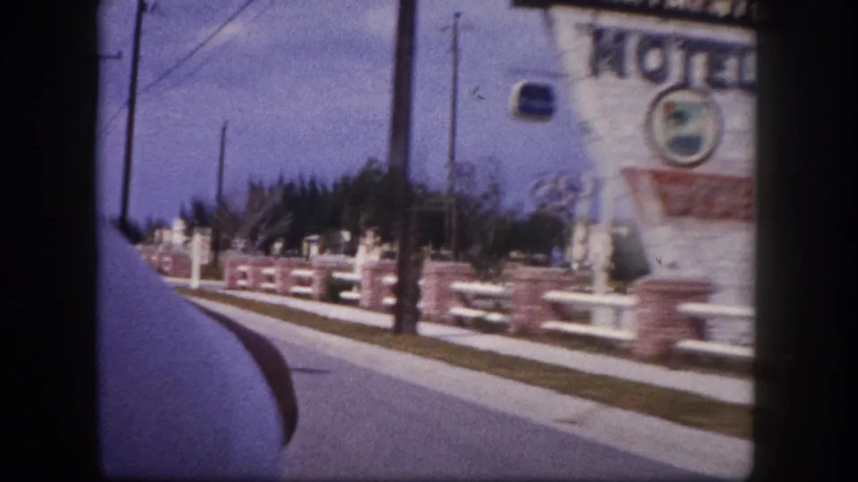 Motion blur fills the frame as the car passes close to the Henri motel sign, with railings, sidewalk, poles, and vehicle edge visible.