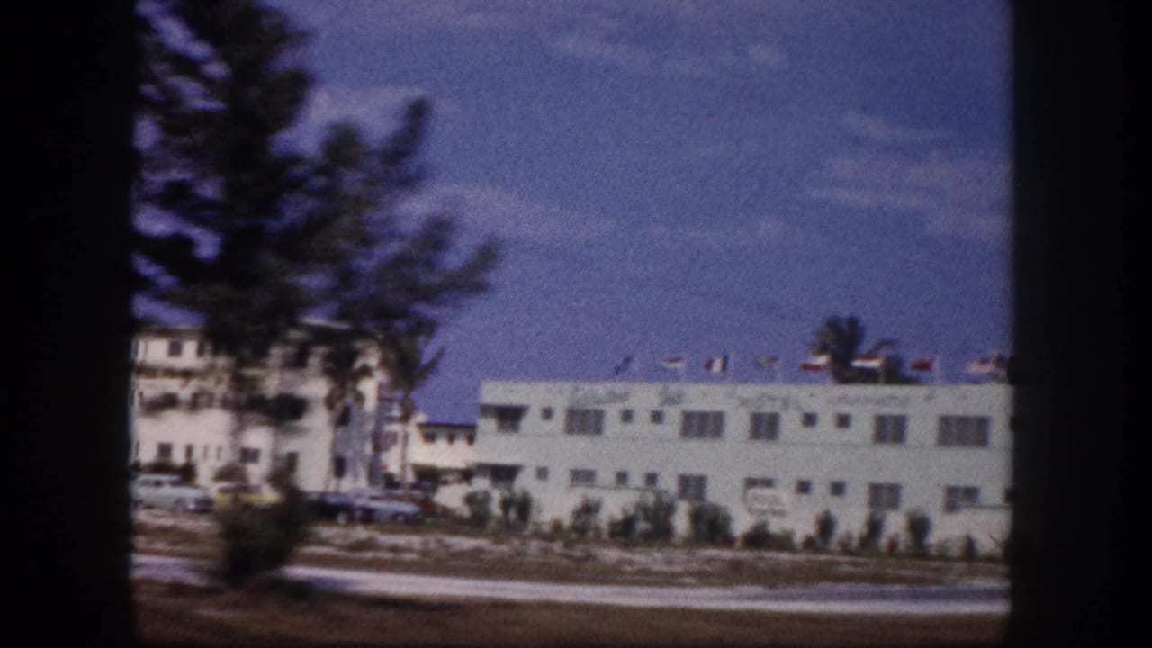 1960 Tampa roadside motel view partly obscured by the film frame edge, showing cars, a palm tree, and white lodging buildings.