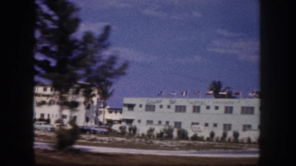 1960 Tampa roadside motel view partly obscured by the film frame edge, showing cars, a palm tree, and white lodging buildings.