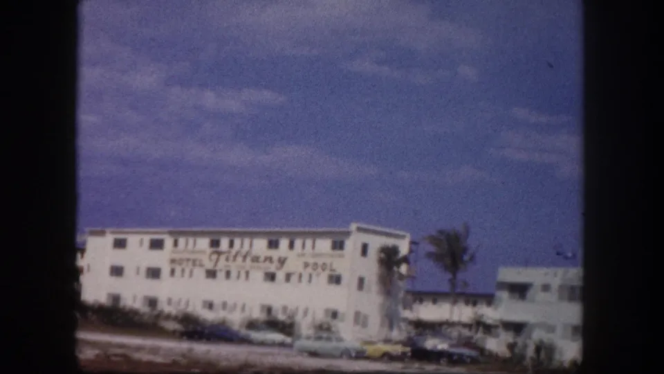 1960 Tampa frame showing the Tiffany Motel name on a white low-rise building, with classic cars and a palm tree along the road.