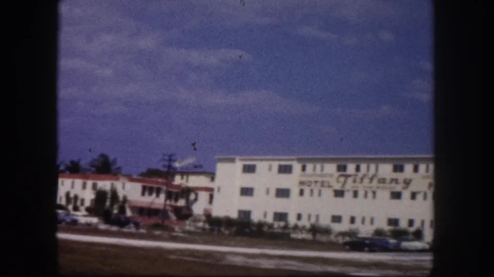 1960 Tampa home-movie frame of the Tiffany Motel facade, with visible sign lettering, roof flags, red trim, and cars along the road.