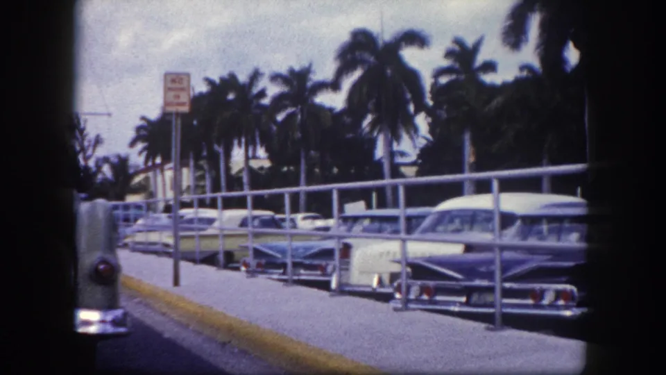 1960 Tampa home-movie view of a parking sign, curbside railings, palms, and classic cars.