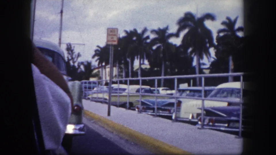 1960 Tampa frame showing railings, parked classic cars, palms, and the edge of a nearby vehicle.