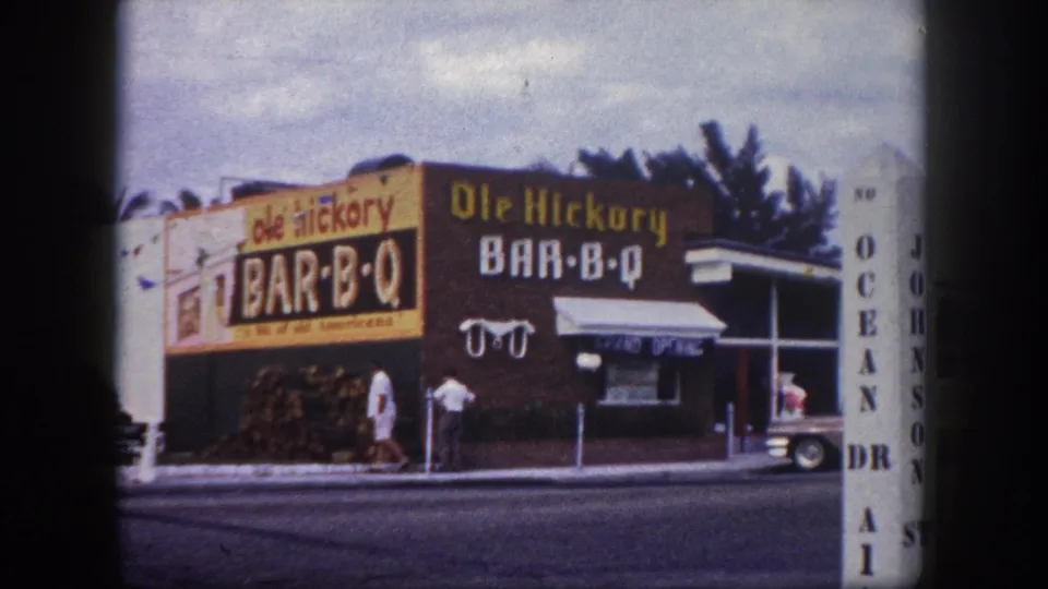 1960 Tampa frame showing Ole Hickory Bar-B-Q signage, people at the entrance, a street foreground, and a vertical Ocean Drive sign at right.