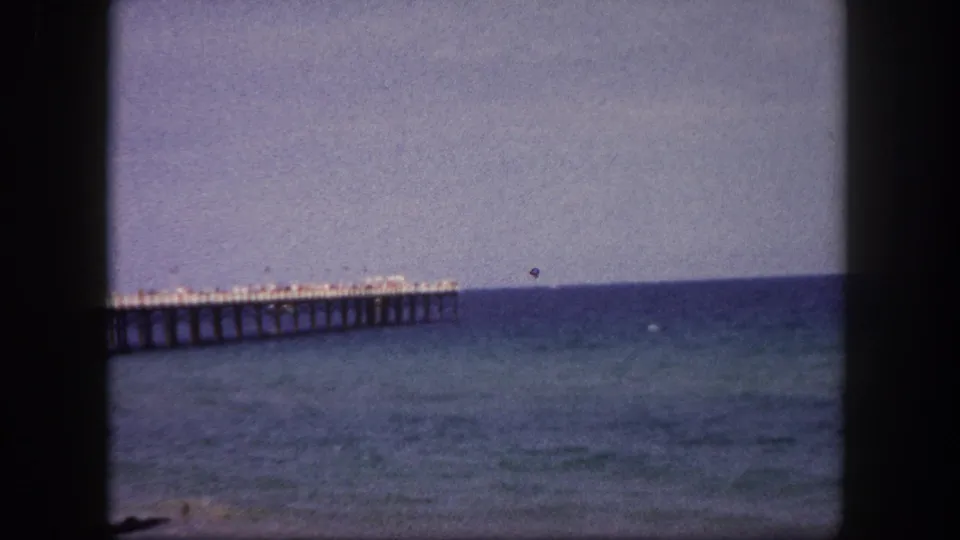 1960 Tampa, Florida beach view with a long pier crossing the water under a hazy sky on 8mm film.