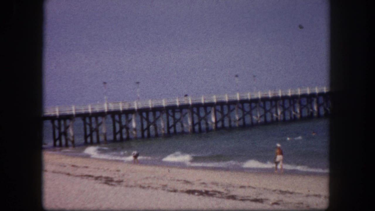 Continuation of the pier-and-beach wide shot with a brightly dressed figure at the water's edge, Tampa, Florida, circa 1960.