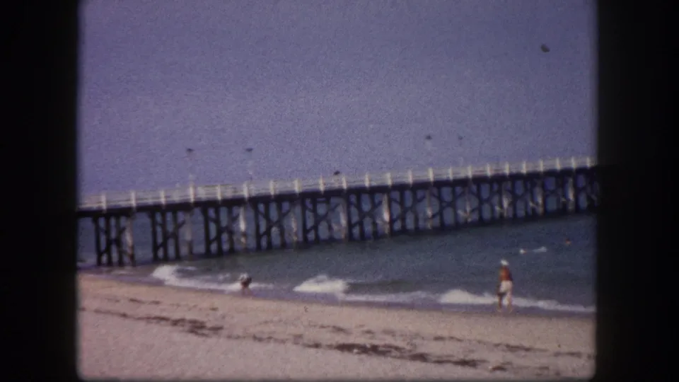 Continuation of the pier-and-beach wide shot with a brightly dressed figure at the water's edge, Tampa, Florida, circa 1960.
