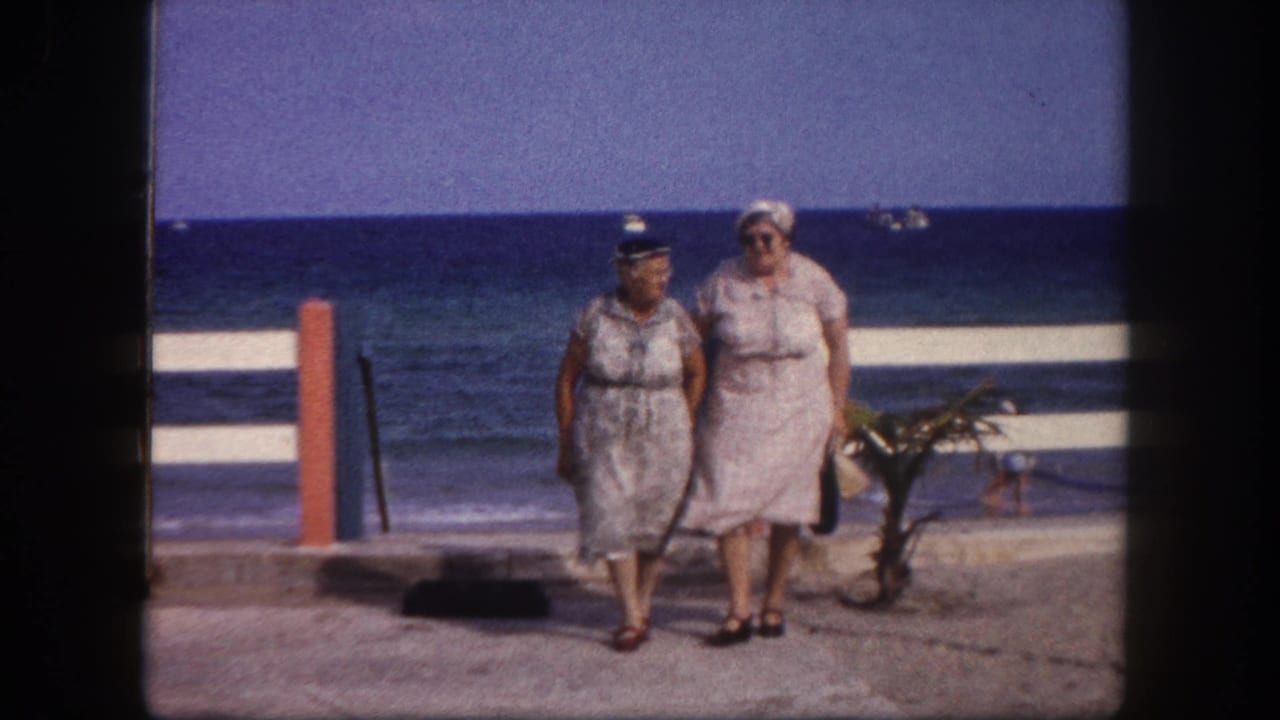 Two adult women in belted summer dresses and white sun hats walk a beachfront promenade; metadata identifies Tampa, Florida, circa 1960.
