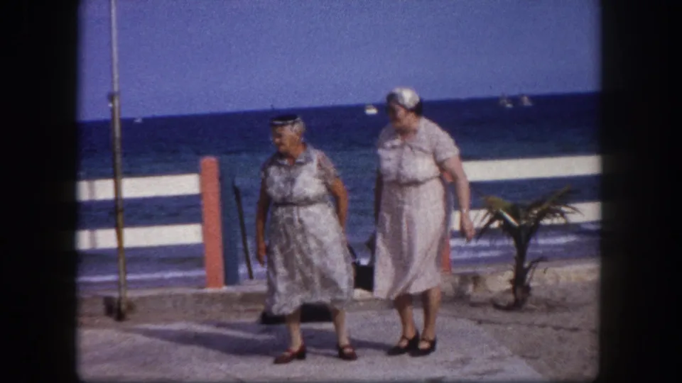 Two women in early-1960s summer attire walk a seafront promenade, likely Tampa, Florida circa 1960, captured on 8mm color film.