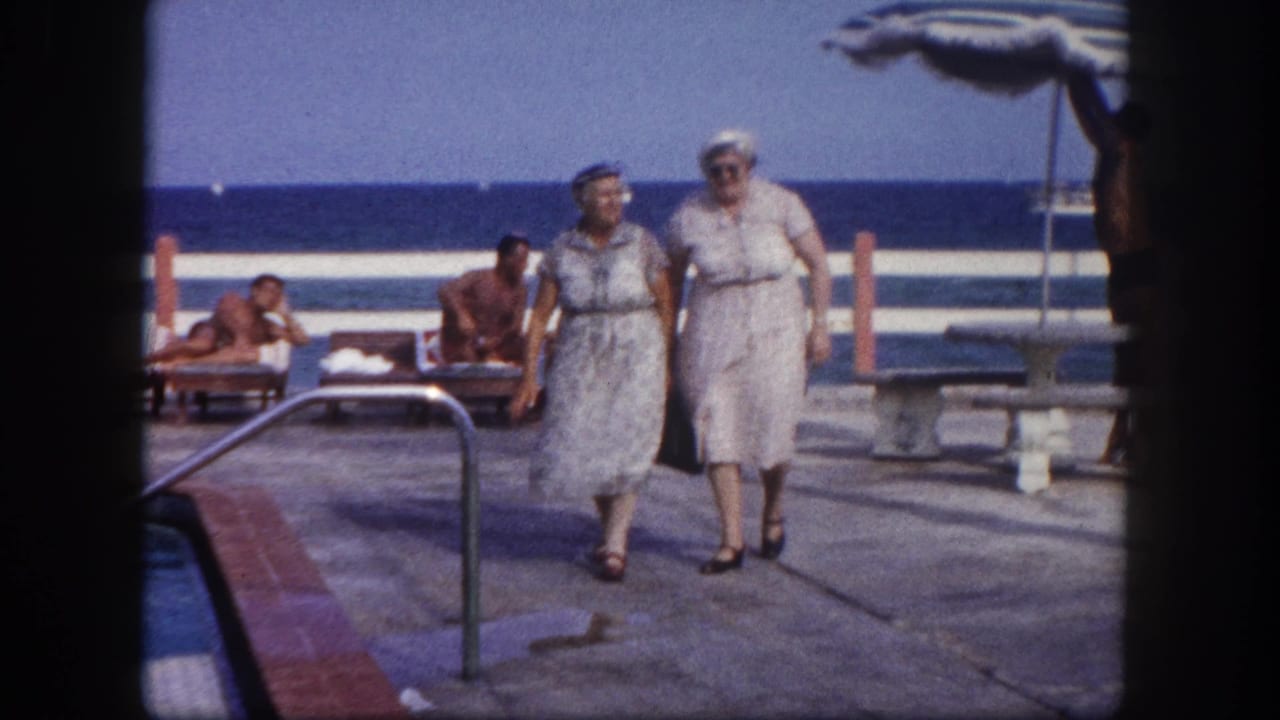 Two older women in early 1960s resort attire walk toward camera on a concrete pool deck at what appears to be a Florida oceanfront resort, circa 1960.