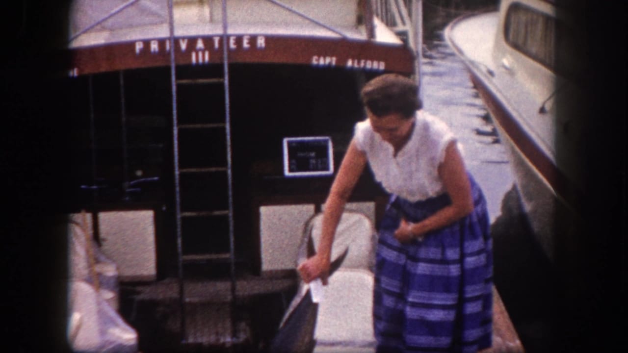 Early 1960s 8mm frame, Tampa Florida — woman in period leisure attire displays a large game fish at a dock; boat stern reads 'PRIVATEER III / CAPT ALFORD'.