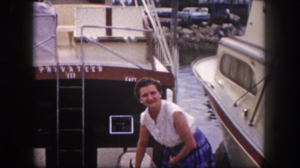 Woman kneels with fishing catch on marina dock beside vessel PRIVATEER III and its boarding ladder, circa 1960 Florida.