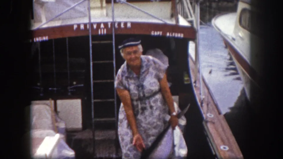 Woman displays a sport fish on a dock with 'PRIVATEER III' and 'CAPT. ALFORD' legible on the boat transom, Florida marina, circa 1960.