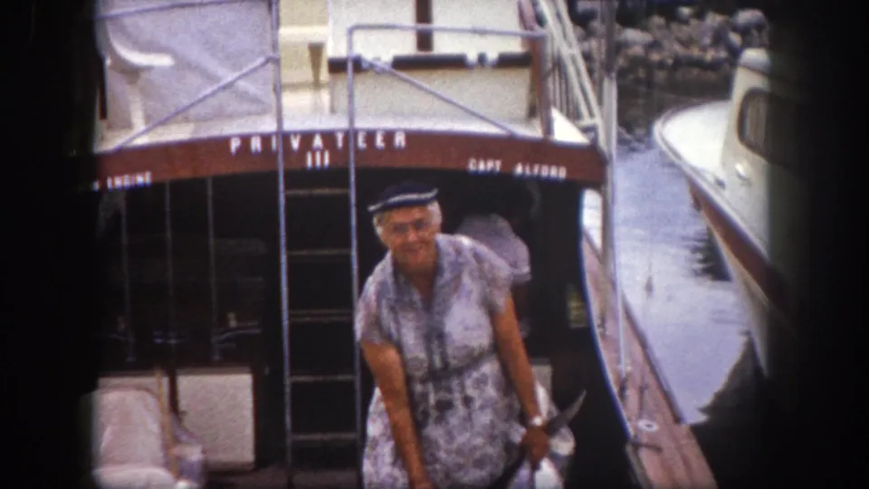 Woman in patterned short-sleeve dress and captain's cap poses on the stern of 'Privateer III' at a Tampa, Florida marina, circa 1960.