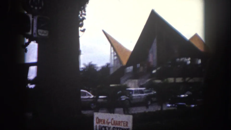 A building with striking angular triangular rooflines — possibly a marina or commercial structure in the Tampa, Florida area circa 1960 — with vintage automobiles and an 'Open 4 Charter' sign visible.