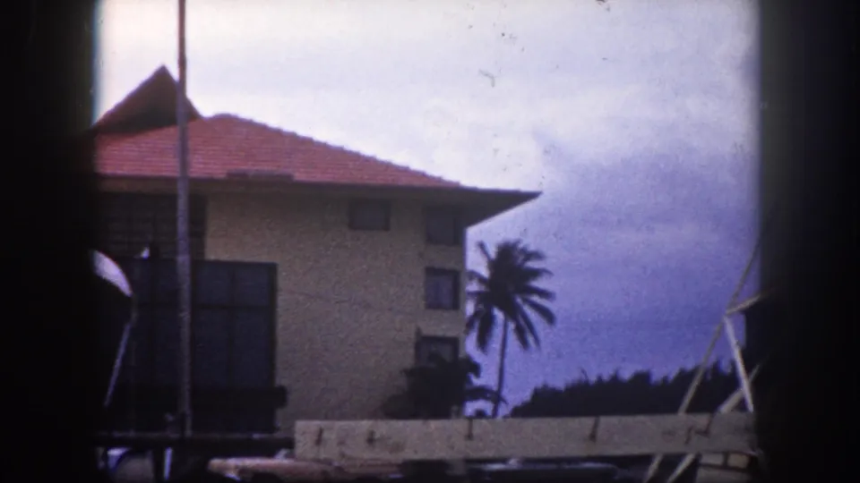 Two-story Florida vernacular building with prominent red tile hip roof and a tall palm tree, Tampa area, circa 1960, 8mm color film.