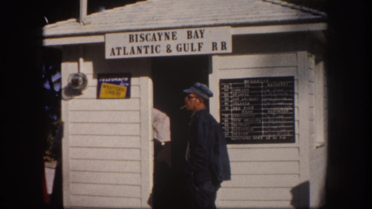 Man at the Biscayne Bay Atlantic & Gulf RR station building, Crandon Park area, Florida, circa 1960; schedule board and branded signage on white clapboard exterior.