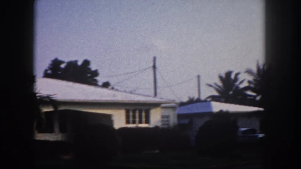 1960 Tampa home-movie frame showing low suburban houses, overhead wires, palm foliage, and heavy dark frame edges.
