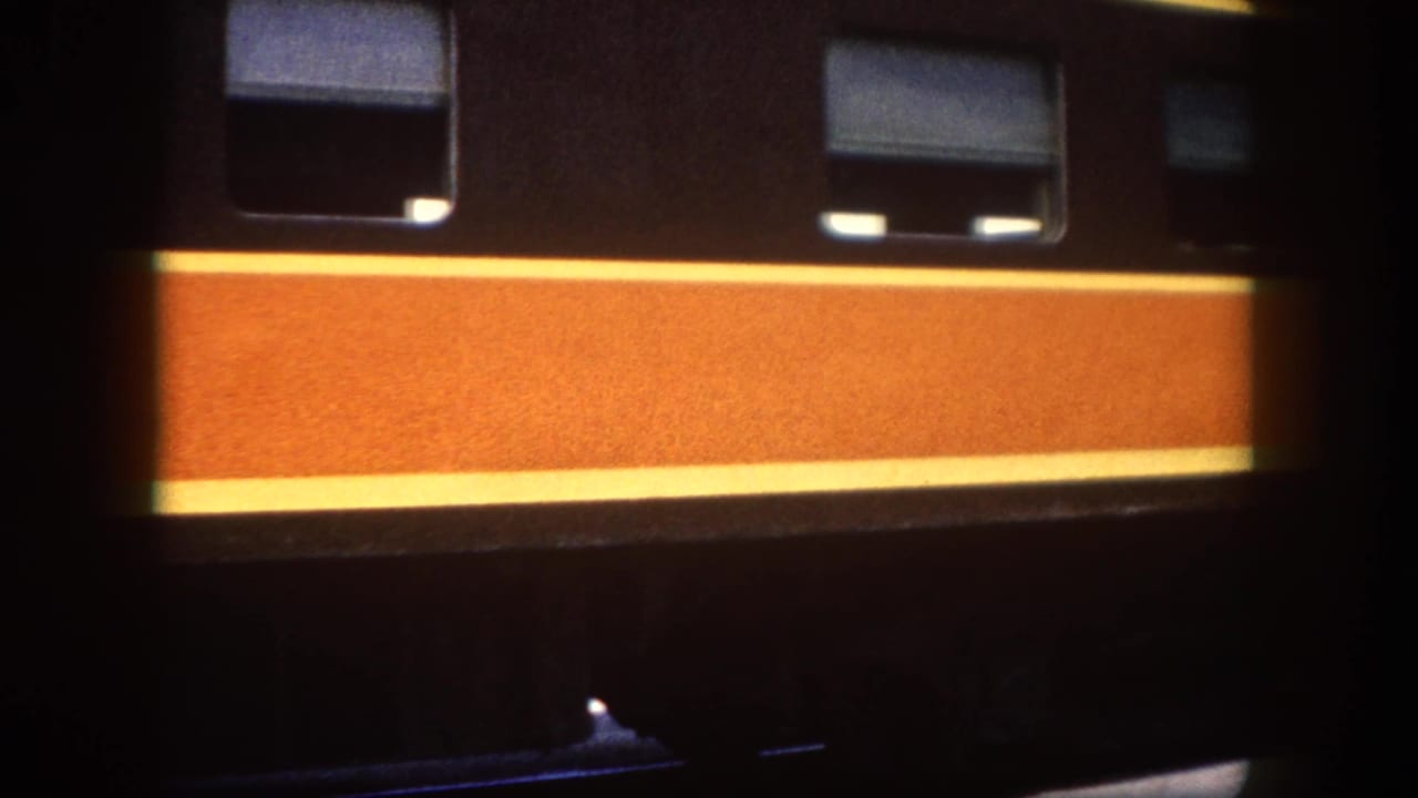 Close-up of a dark passenger train car with a bold orange and yellow horizontal stripe; rectangular windows visible at top.