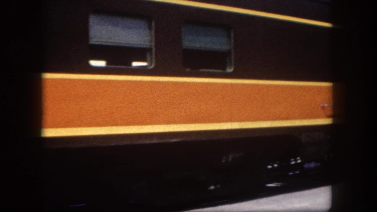 Panning shot continuing along the dark railcar with orange and yellow livery, Tampa, Florida, circa 1960; characteristic 8mm gate vignetting visible.