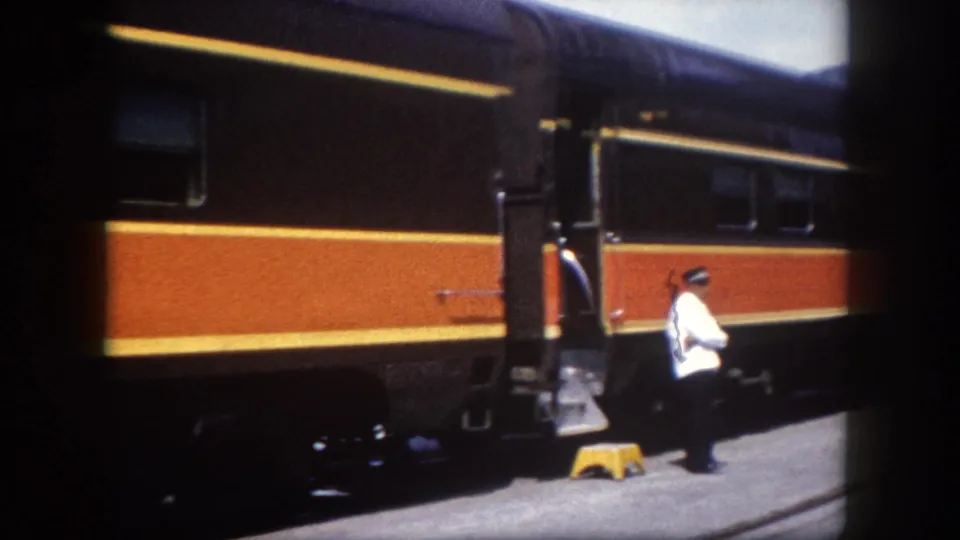 Porter in white uniform at the vestibule steps of an orange-striped passenger railcar on the station platform, Tampa, Florida, circa 1960.
