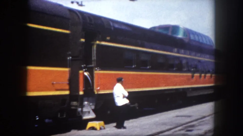 Railroad porter in white uniform beside the orange-striped railcar at a Tampa, Florida station, circa 1960; dome car and open sky visible in background.