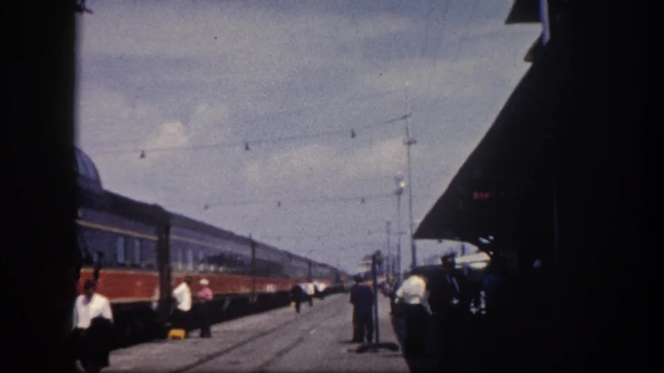 8mm wider view of Tampa station platform, circa 1960; station canopy, overhead wire poles, and multiple period figures including a uniformed attendant visible.