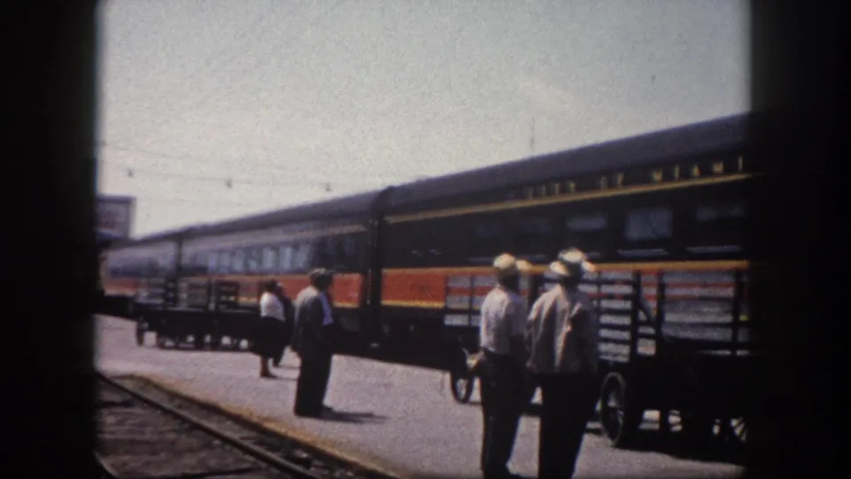 1960 Florida station platform: workers in straw hats beside City of Miami named train cars, a baggage handcart on the concrete platform in bright sunlight.