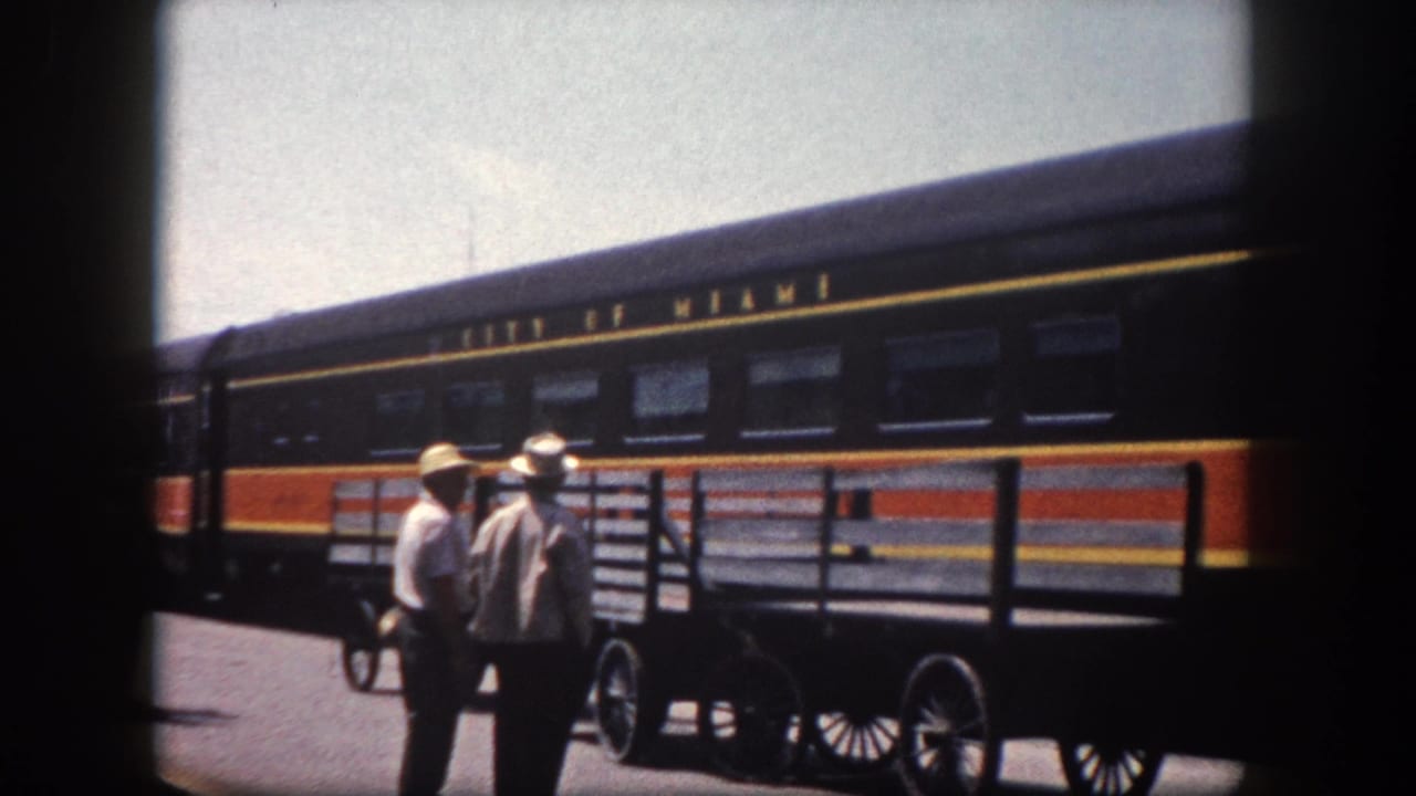 Two men in light shirts and wide-brimmed hats beside a spoked-wheel baggage cart, with the 'City of Miami' passenger railcar at a Tampa-area station, circa 1960.