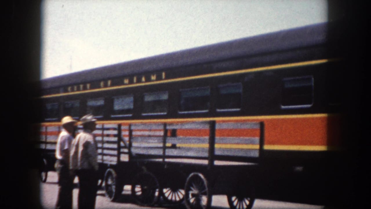 Platform-level view of two men beside a wheeled baggage cart with the boldly striped 'City of Miami' railcar; Tampa-area station, circa 1960.