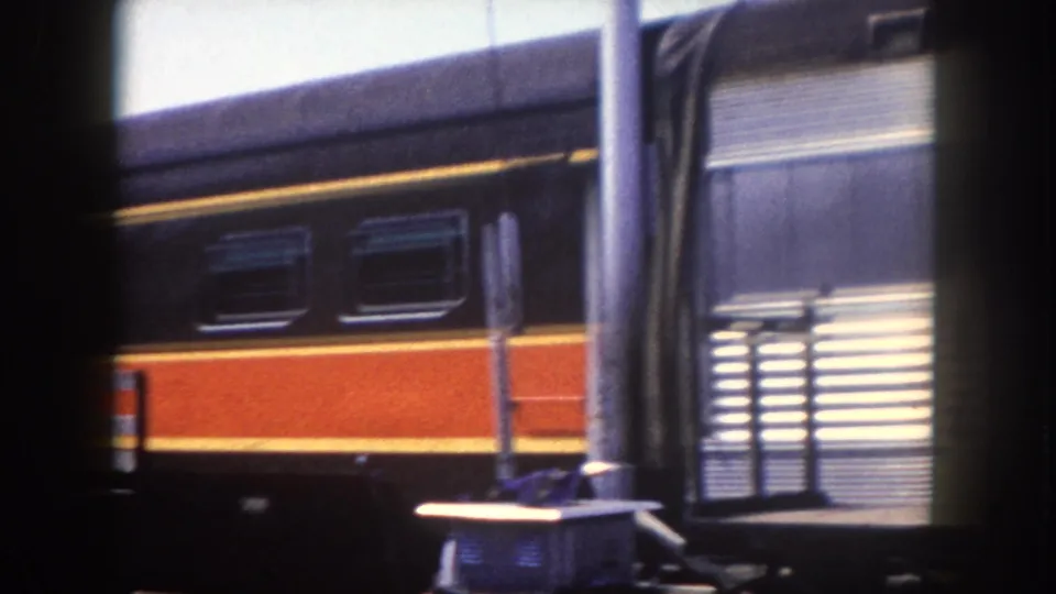 Low-angle detail of the 'City of Miami' passenger car's orange and yellow livery; a metal vent stack and station outbuilding appear at lower right; Tampa area, circa 1960.