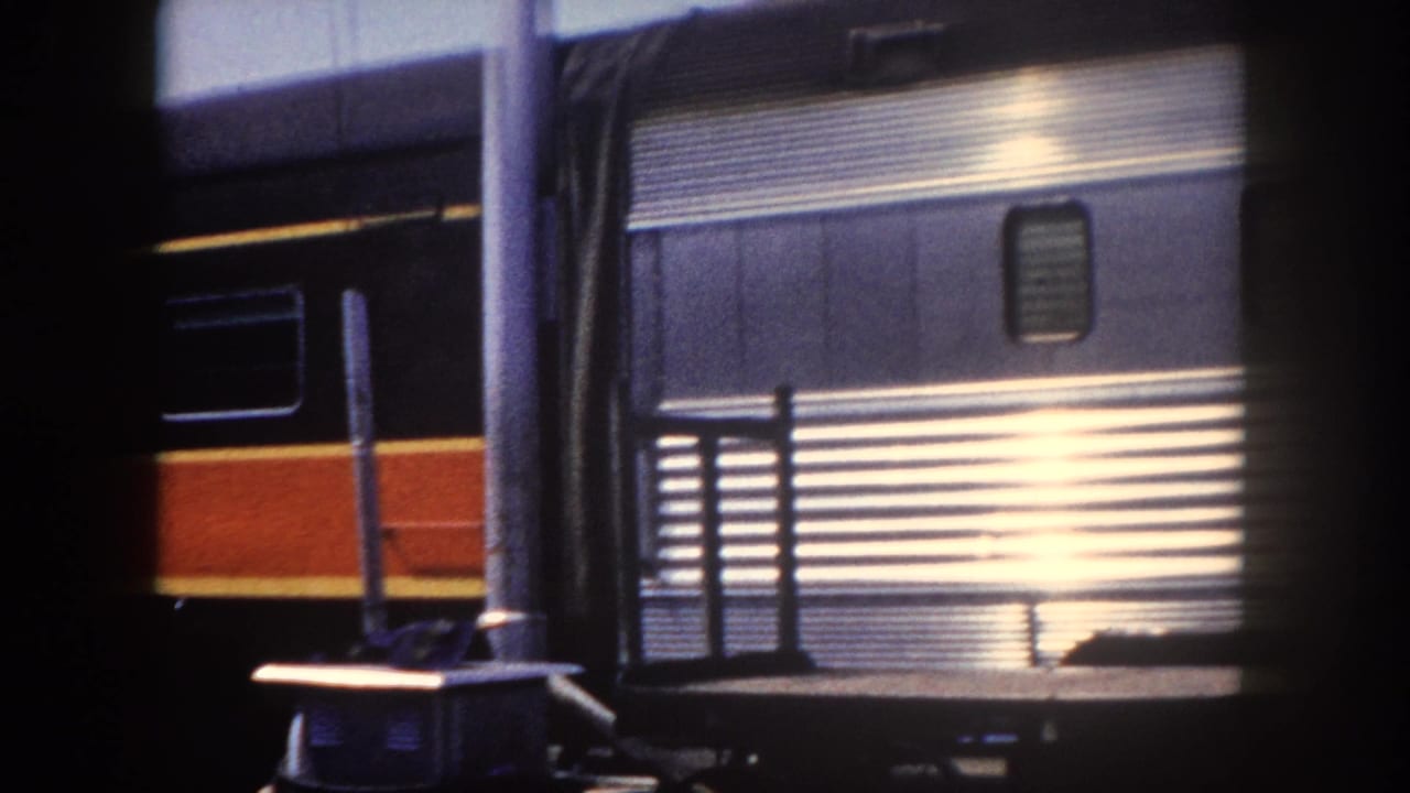 Fluted stainless steel passenger railcar at Tampa station, c. 1960, with strong sunlight flare on polished surface and a second train at far left.