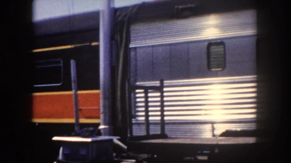 Fluted stainless steel passenger railcar at Tampa station, c. 1960, with strong sunlight flare on polished surface and a second train at far left.