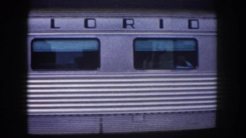 1960 Tampa area: close-up of stainless-steel passenger railcar side bearing partial 'FLORIDA' car name, shot on 8mm film with characteristic grain and blue cast.