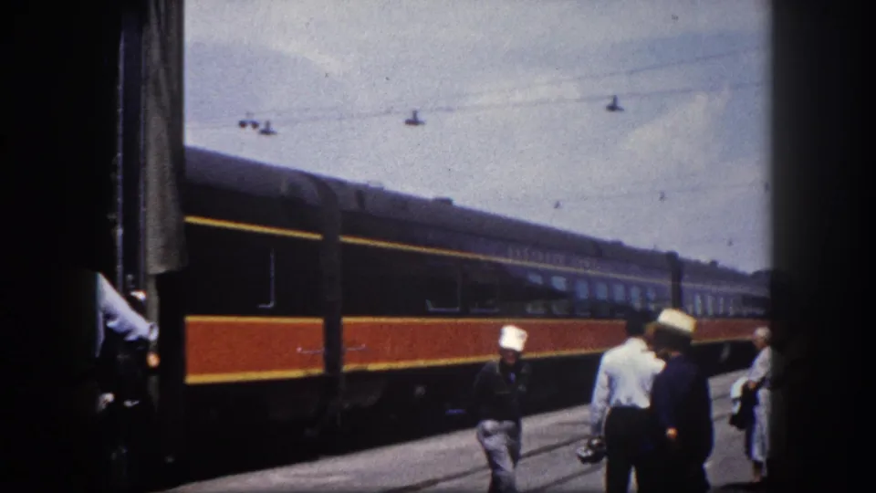View from Tampa station platform showing a dark red and gold Illinois Central passenger car moving past, with a station pillar partially obscuring the foreground