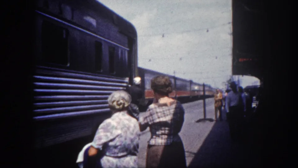 8mm platform view circa 1960, Tampa Florida: two women in period summer dresses stand alongside the stopped passenger train, the car extending toward the horizon.