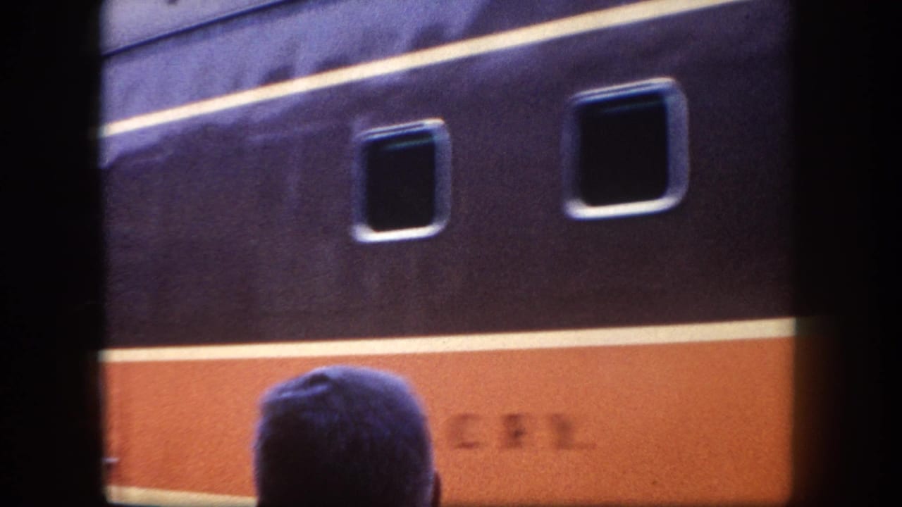 8mm frame of a dark navy and orange passenger car mid-section with partial alphanumeric lettering on the orange band and a waiting passenger in the foreground, Tampa, Florida, circa 1960.