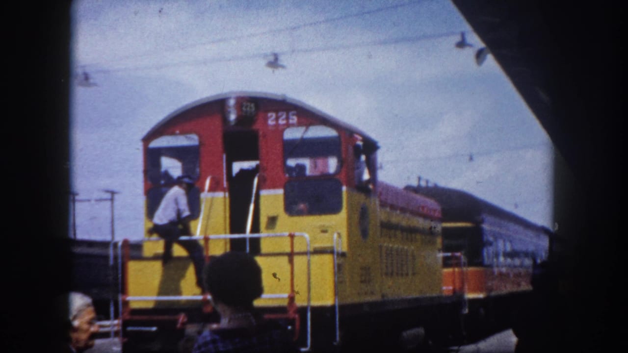 Red and yellow diesel locomotive numbered 225 at a station platform; a man in a white shirt climbs the steps to the cab.