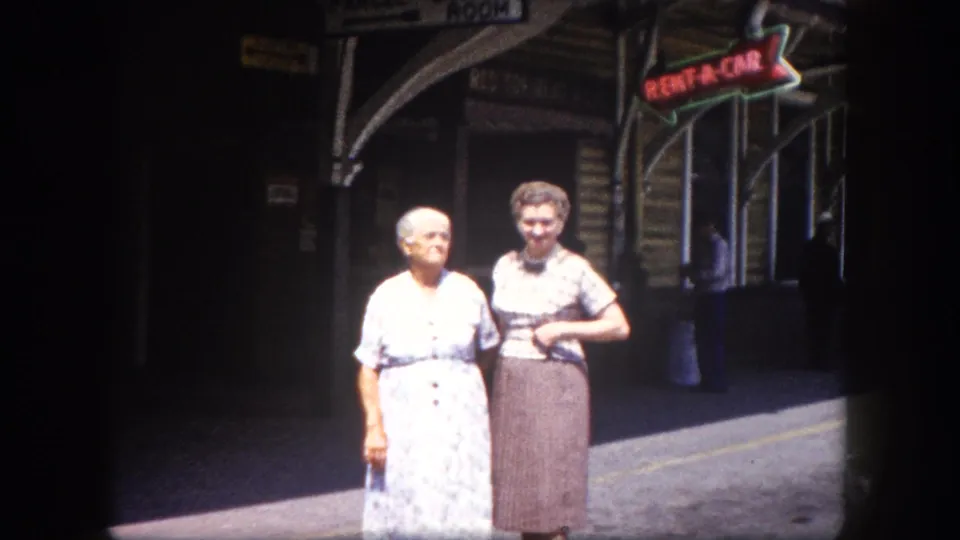 Two elderly women photographed outside what appears to be Tampa's train station depot, circa 1960; neon RENT-A-CAR sign prominent at upper right, arched facade behind.