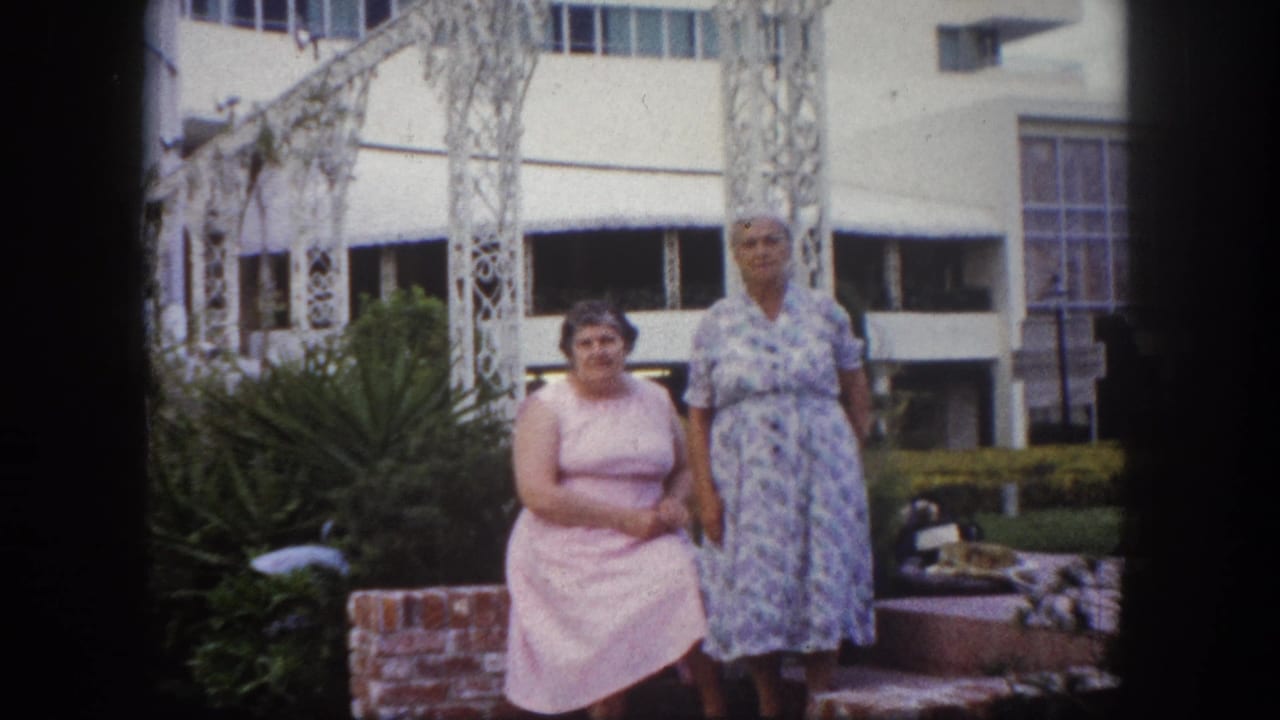 Two women standing together before white ornate metalwork and a mid-century modern building exterior, Tampa, Florida, circa 1960, 8mm film.